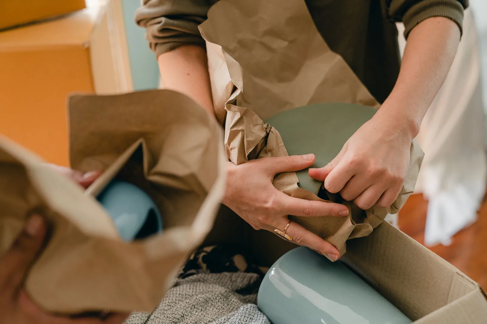 Due mani avvolgono un oggetto di ceramica nella carta da imballo sopra uno scatolone aperto