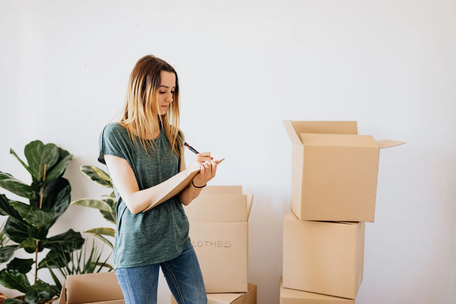 A young woman takes notes on a clipboard next to cardboard boxes ready for the move