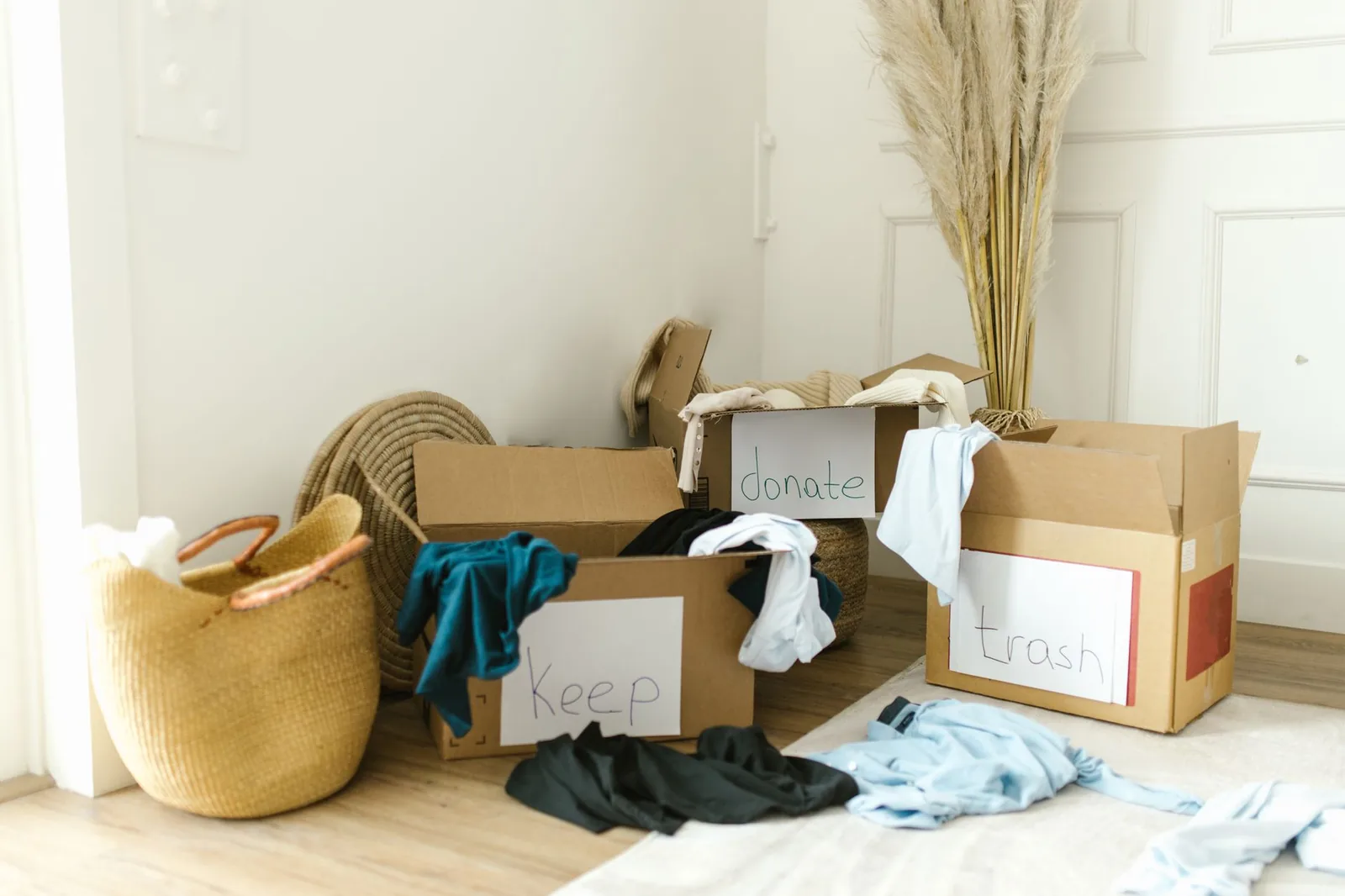 Three cardboard boxes with keep, donate and trash signs, full of clothes to sort