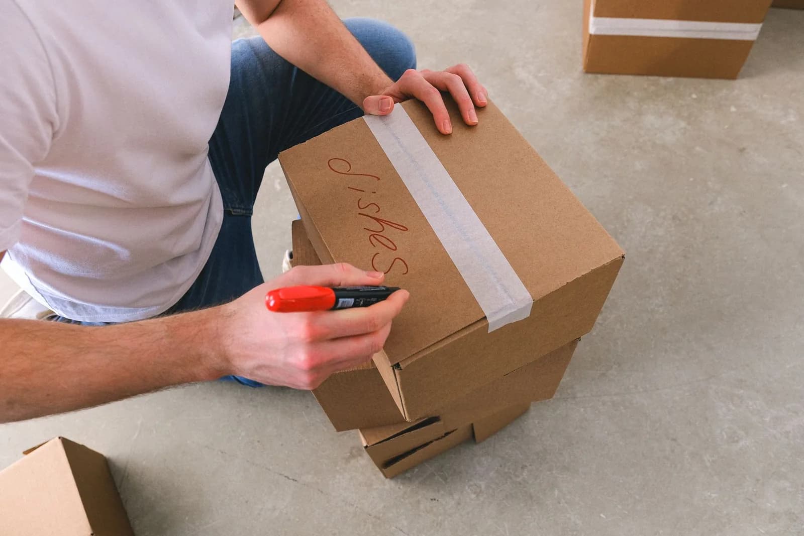 A hand writing with a red marker on top of a cardboard box