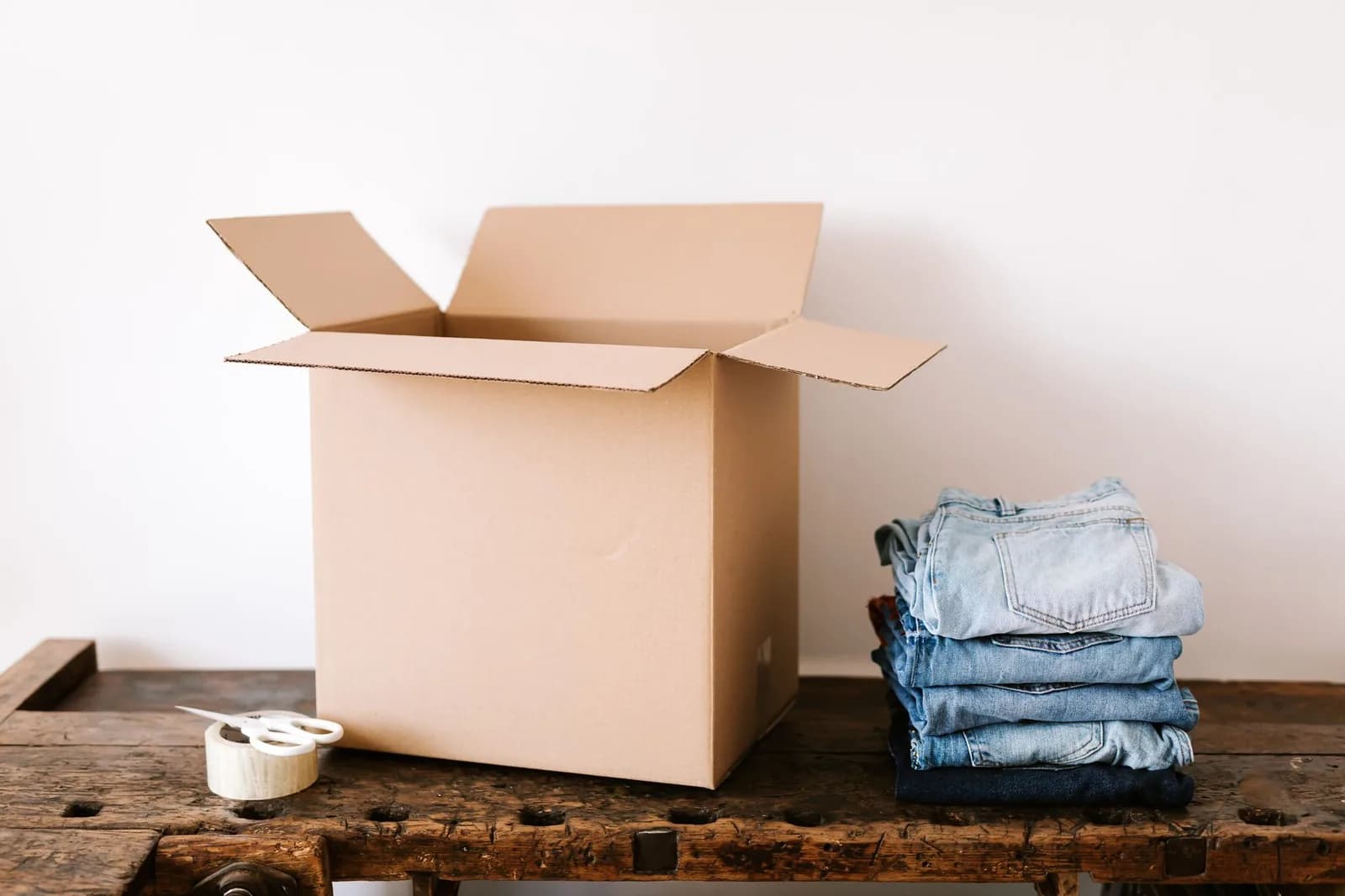 Jeans piegati accanto a uno scatolone aperto e a un rotolo di nastro adesivo