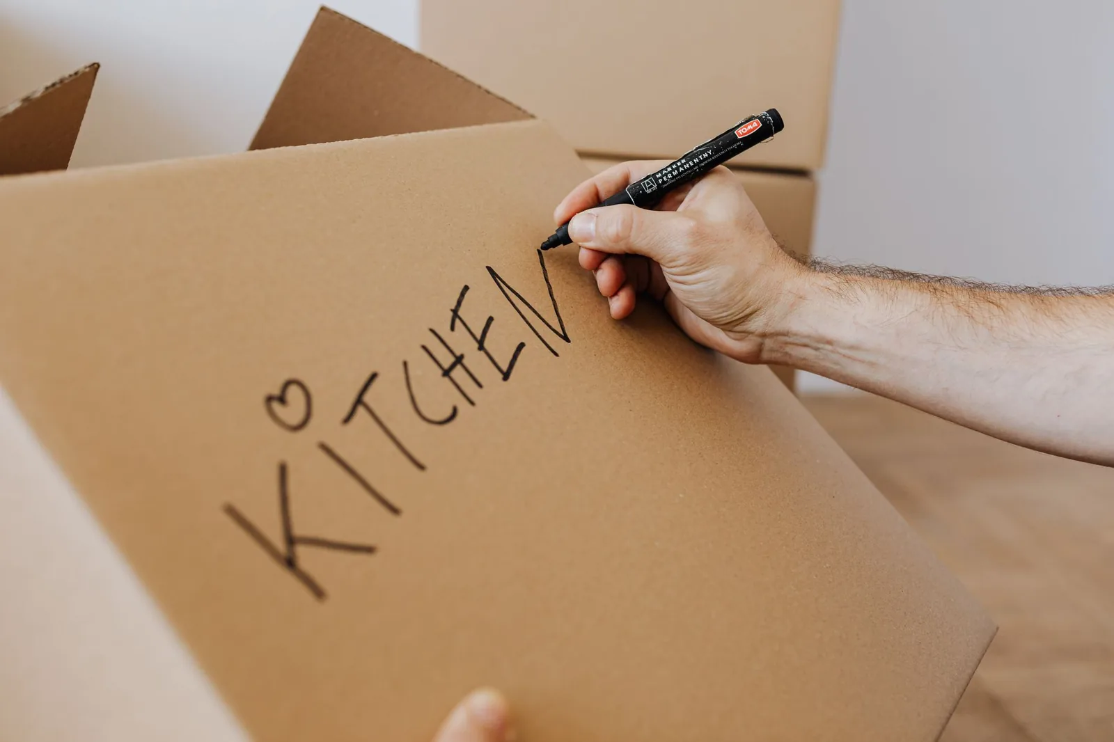 Una mano scrive con il pennarello nero la parola Kitchen sul lato di uno scatolone di cartone