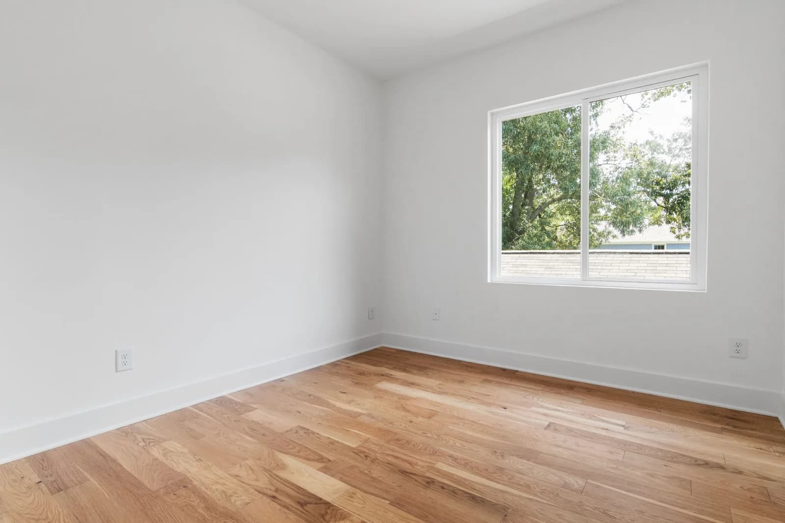 Una stanza vuota con il parquet e una finestra sugli alberi
