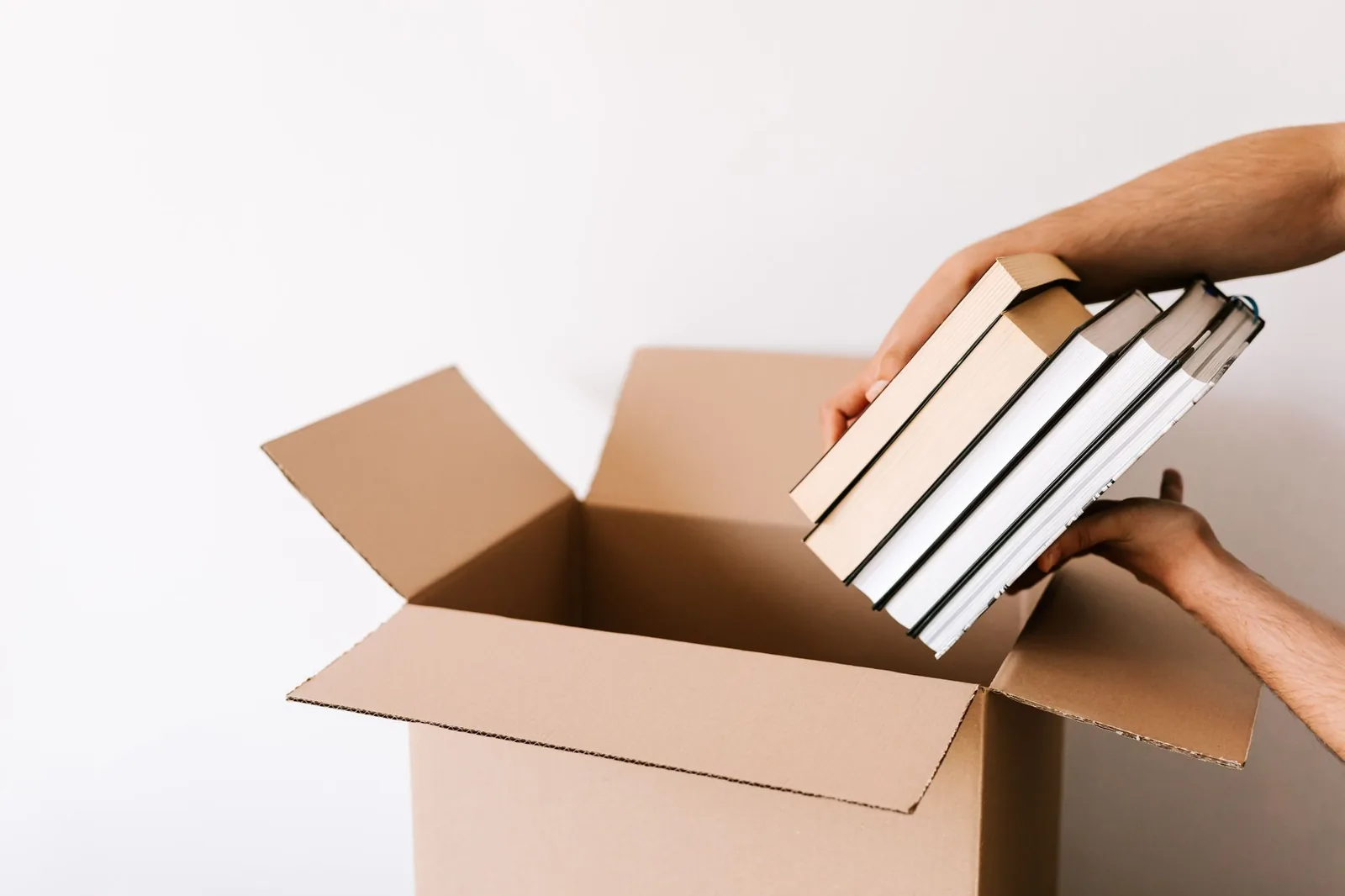 Due mani mettono una pila di libri in uno scatolone aperto