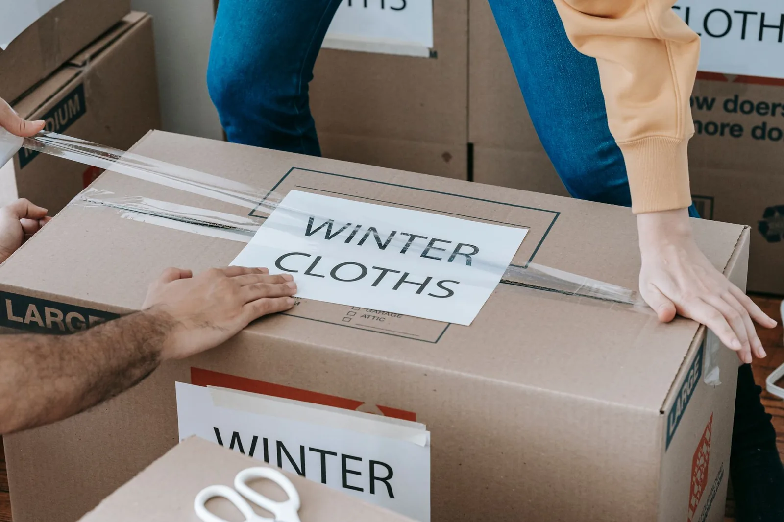 Due persone chiudono con il nastro uno scatolone con l'etichetta dei vestiti invernali