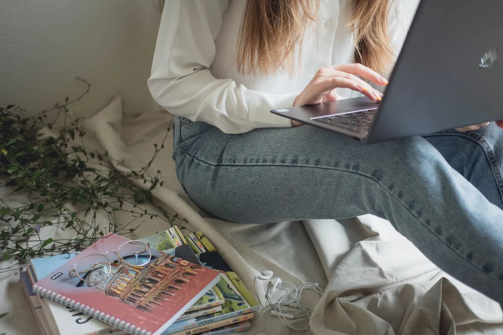 Una studentessa al computer portatile, seduta accanto a una pila di libri di lingue