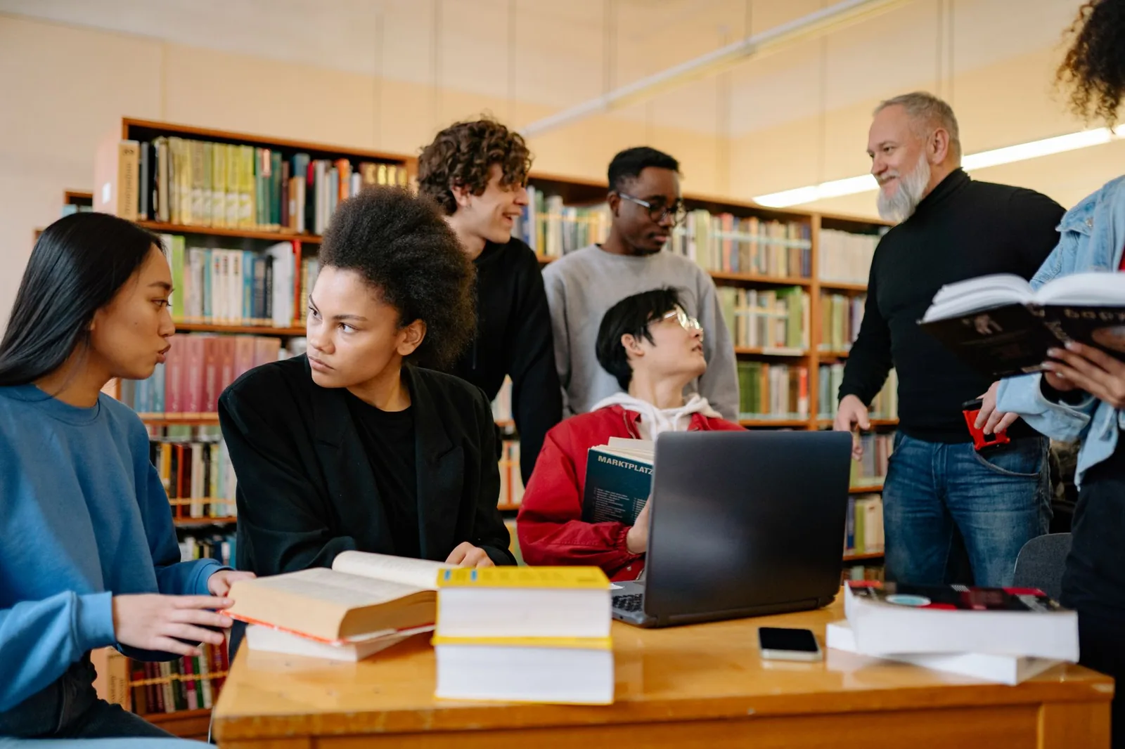 Studenti seduti a un tavolo in biblioteca, circondati da libri e computer portatili.