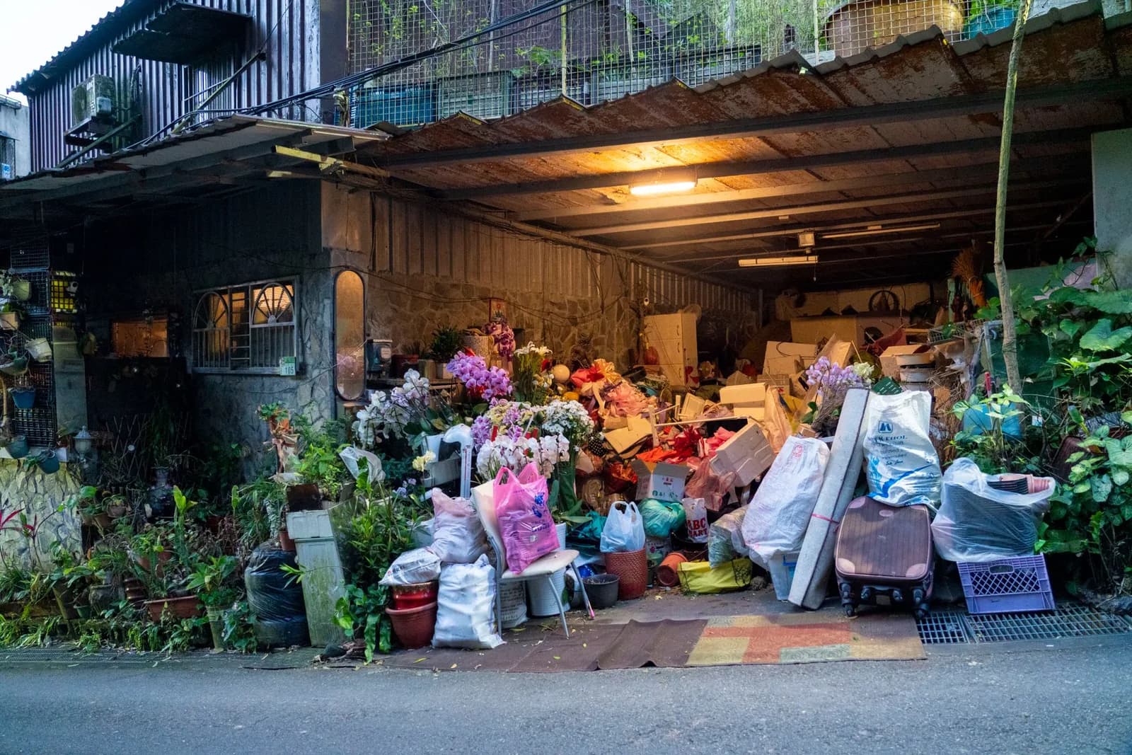 Un garage di casa pieno fino all'ingresso, con scatole, piante e sacchi accatastati.