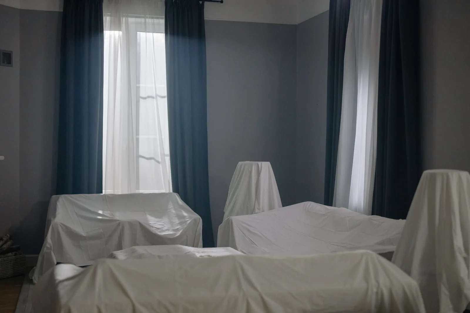 Stanza in penombra con i mobili coperti da teli bianchi.