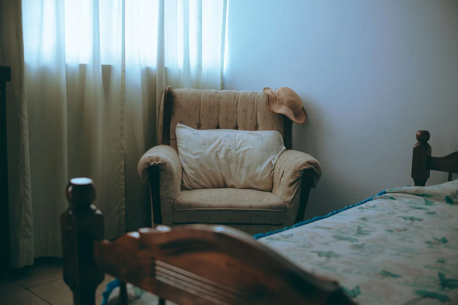 Poltrona antica accanto a una finestra con tende chiare, in una camera.
